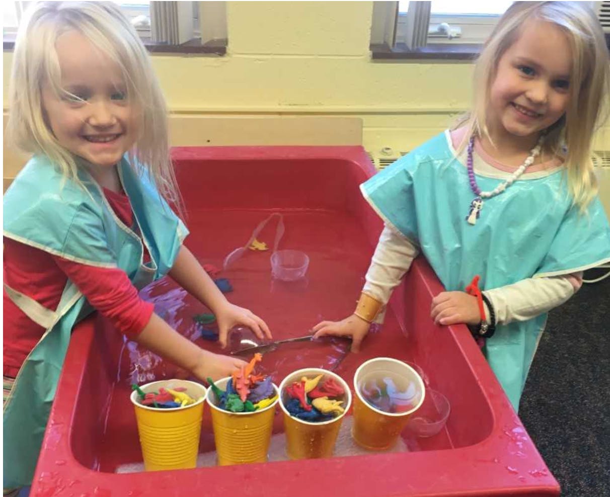 Two children playing in a water table with cups and toys