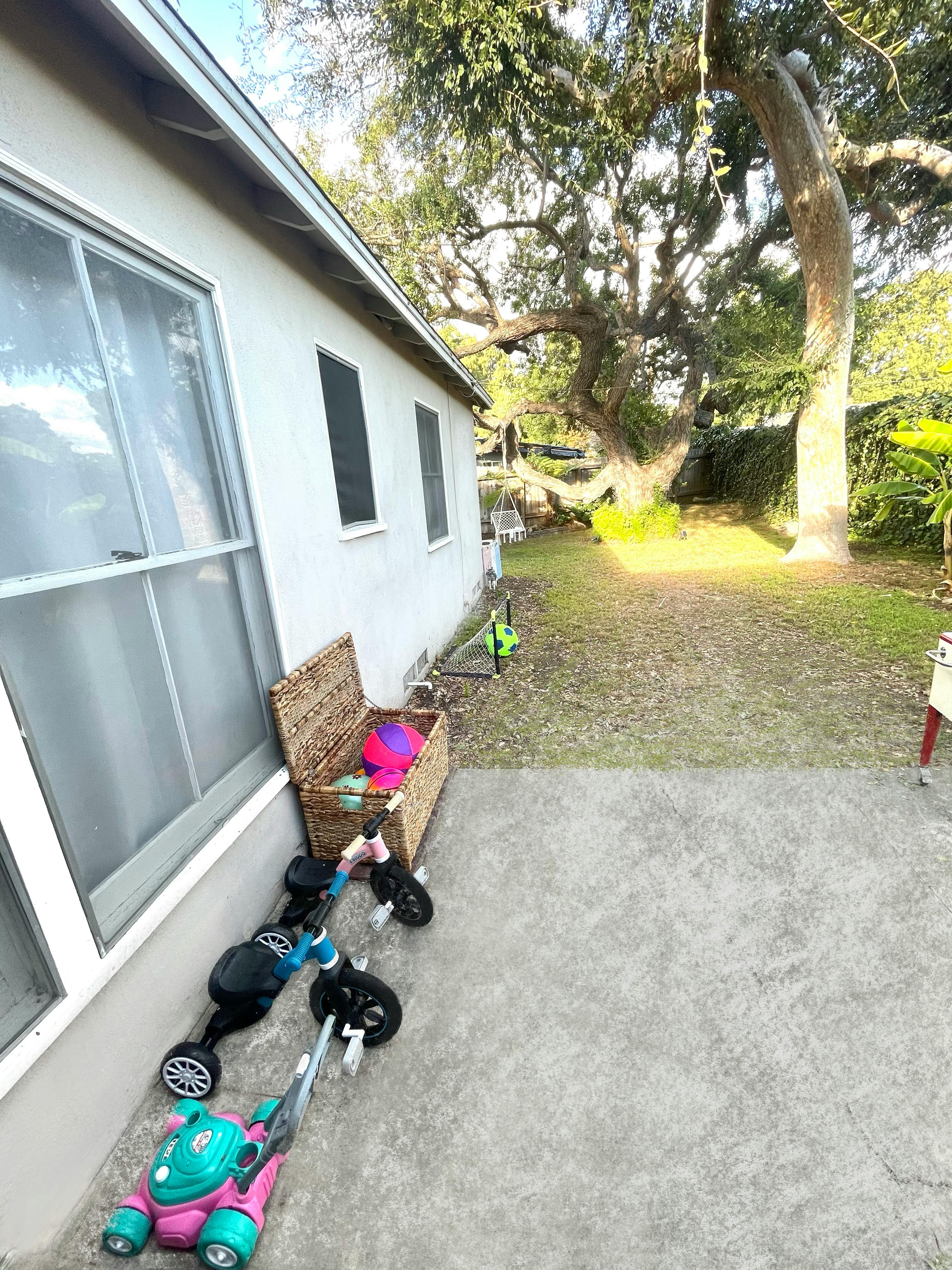 House exterior with toys on a patio next to a large tree