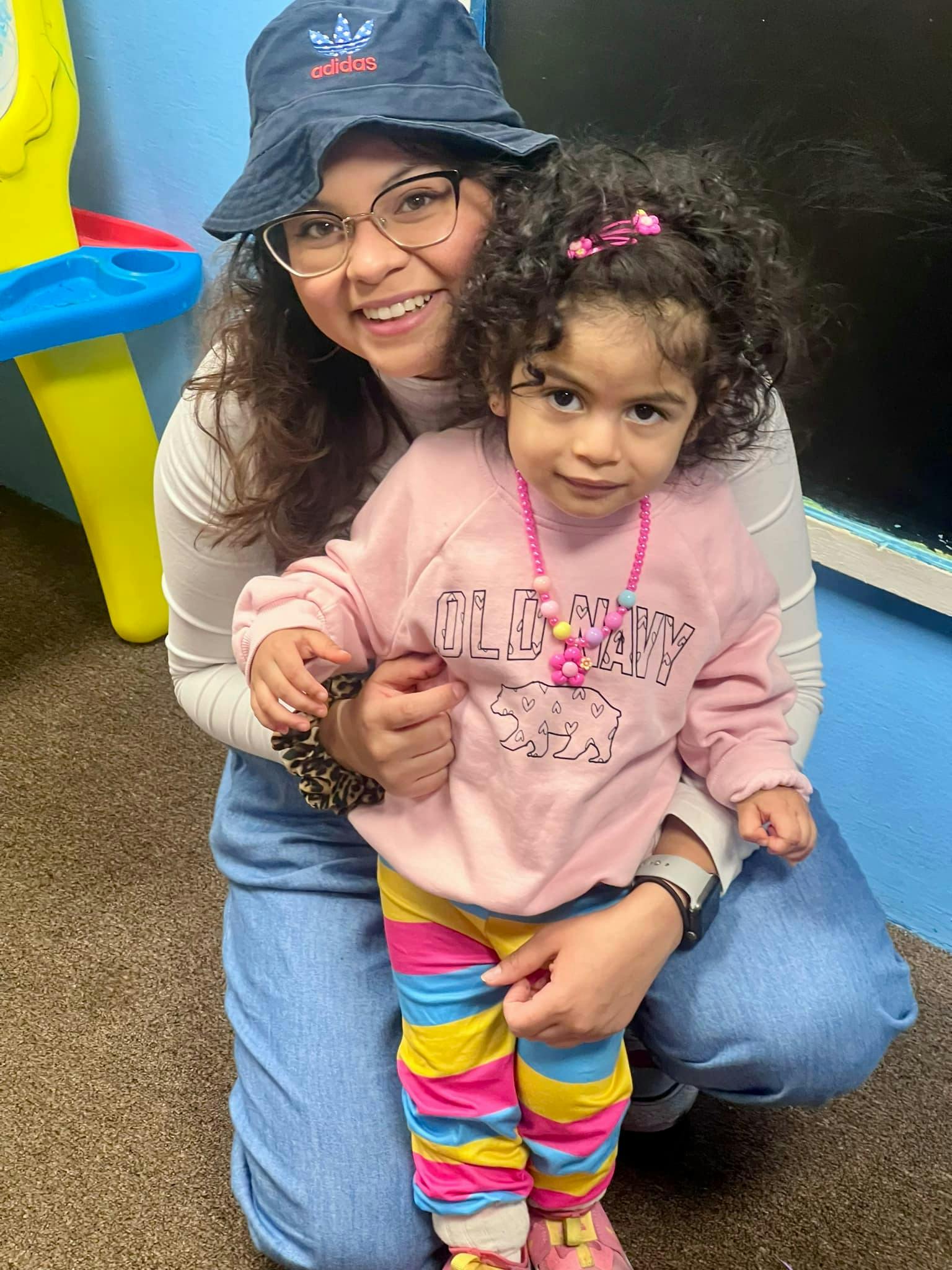 Person in a bucket hat holding a child in a pink Old Navy sweatshirt