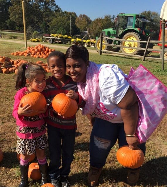 Person and two children holding pumpkins in a field