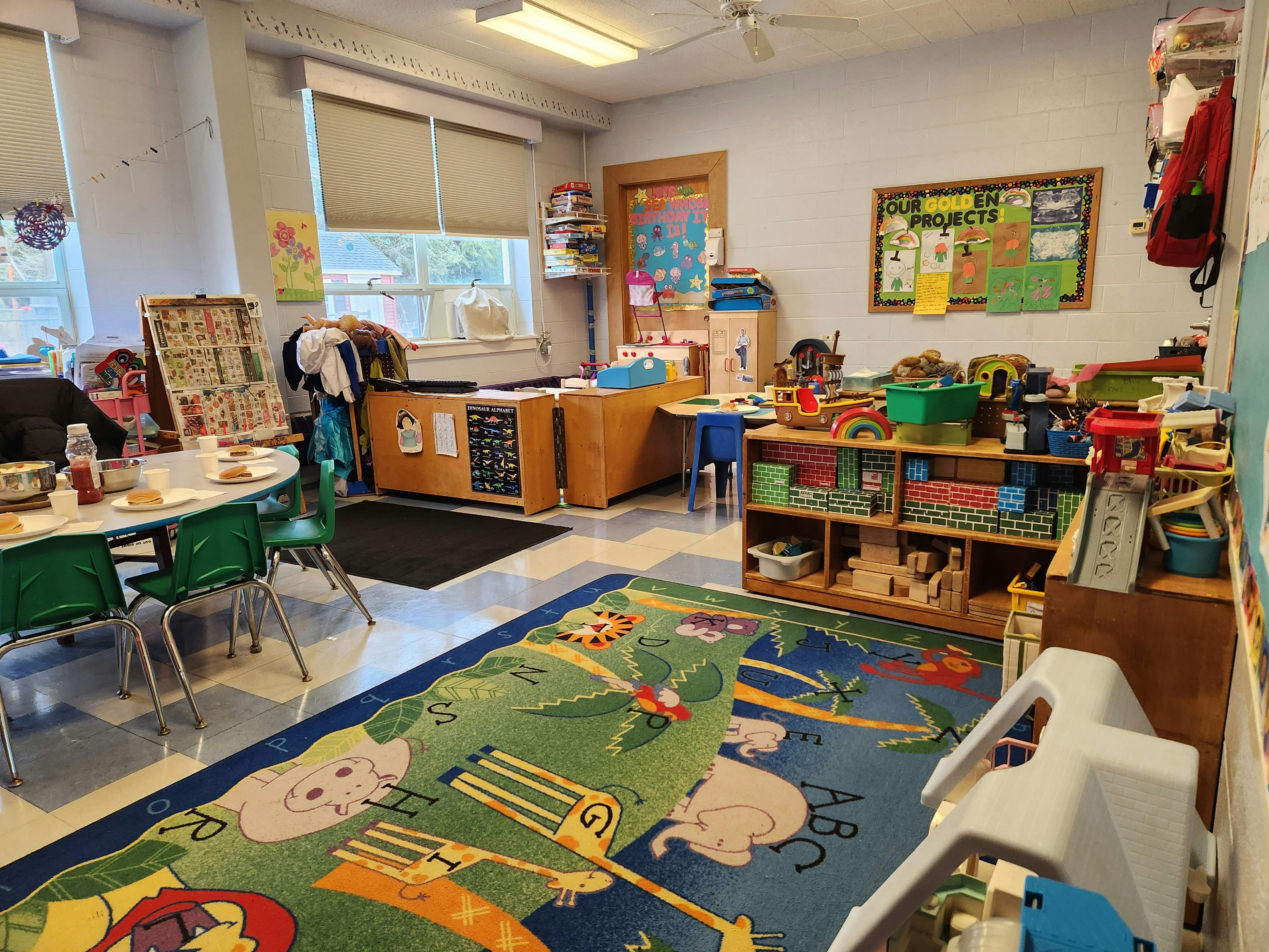A classroom with a colorful rug, tables, chairs, and shelves