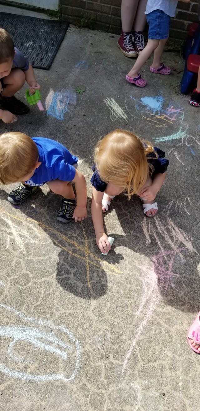 Two children drawing with chalk on pavement