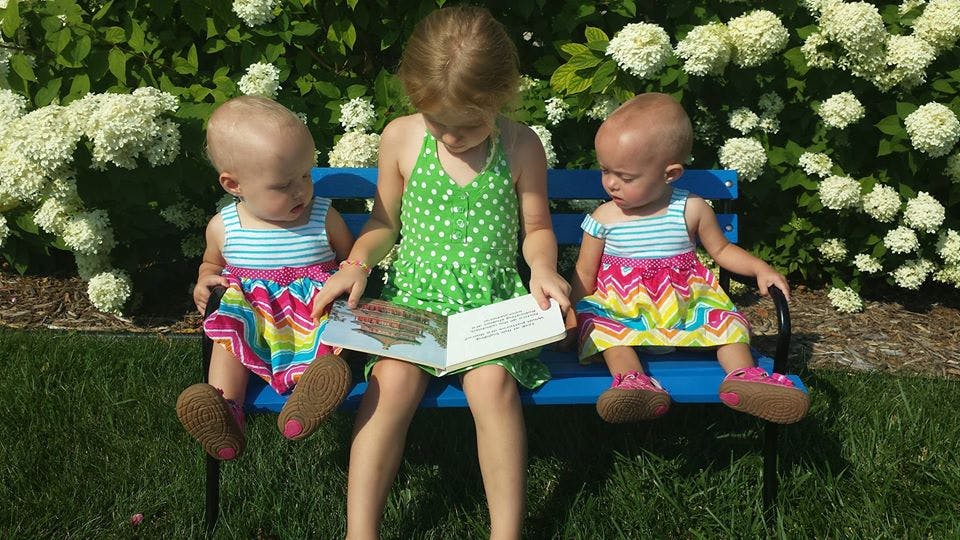 Child reading a book to two babies on a bench