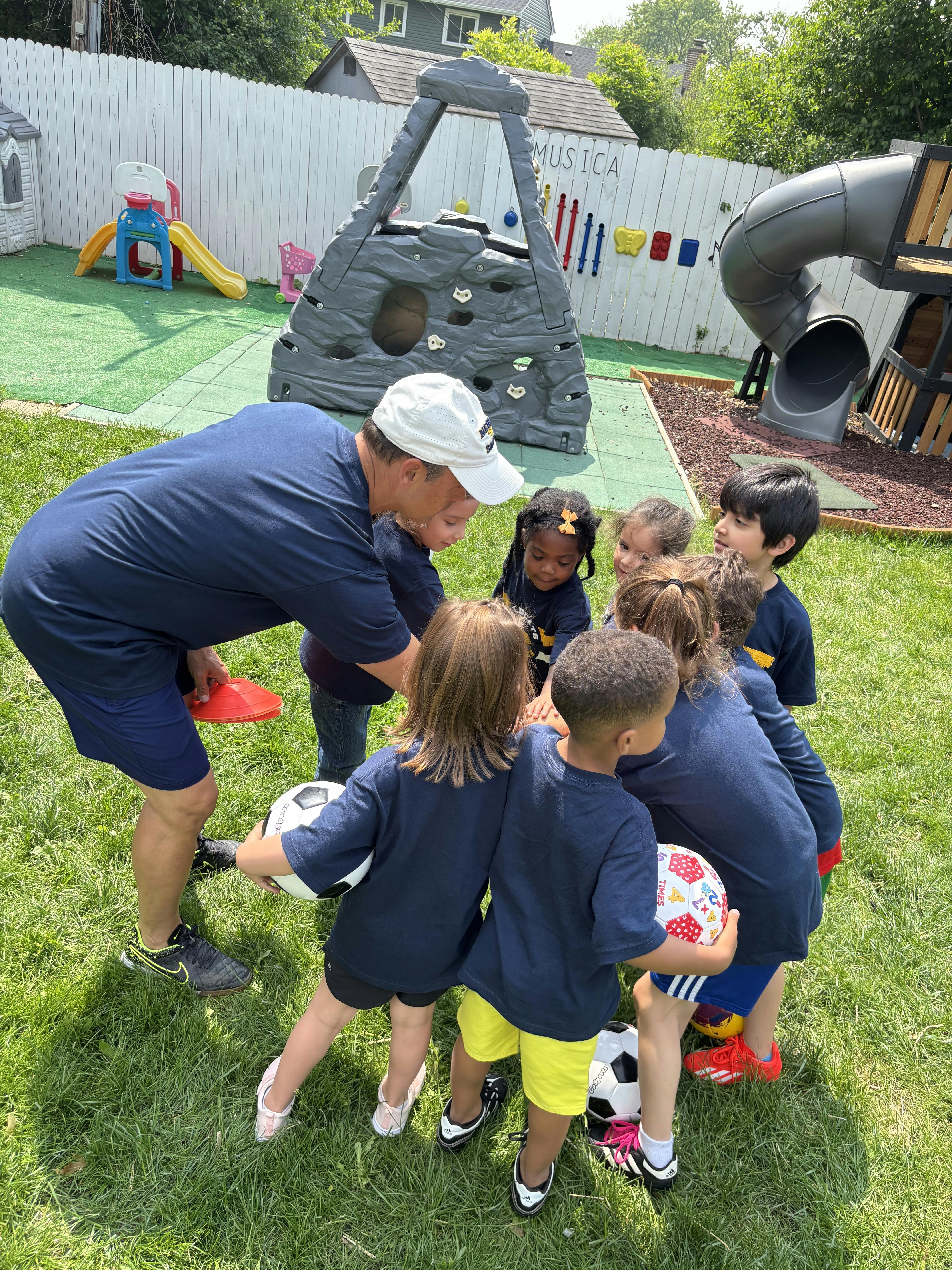 Adult with multiple children holding soccer balls