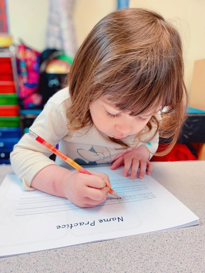 Child writing on a "Name Practice" worksheet with a pencil