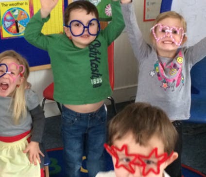 Children wearing novelty glasses with arms raised