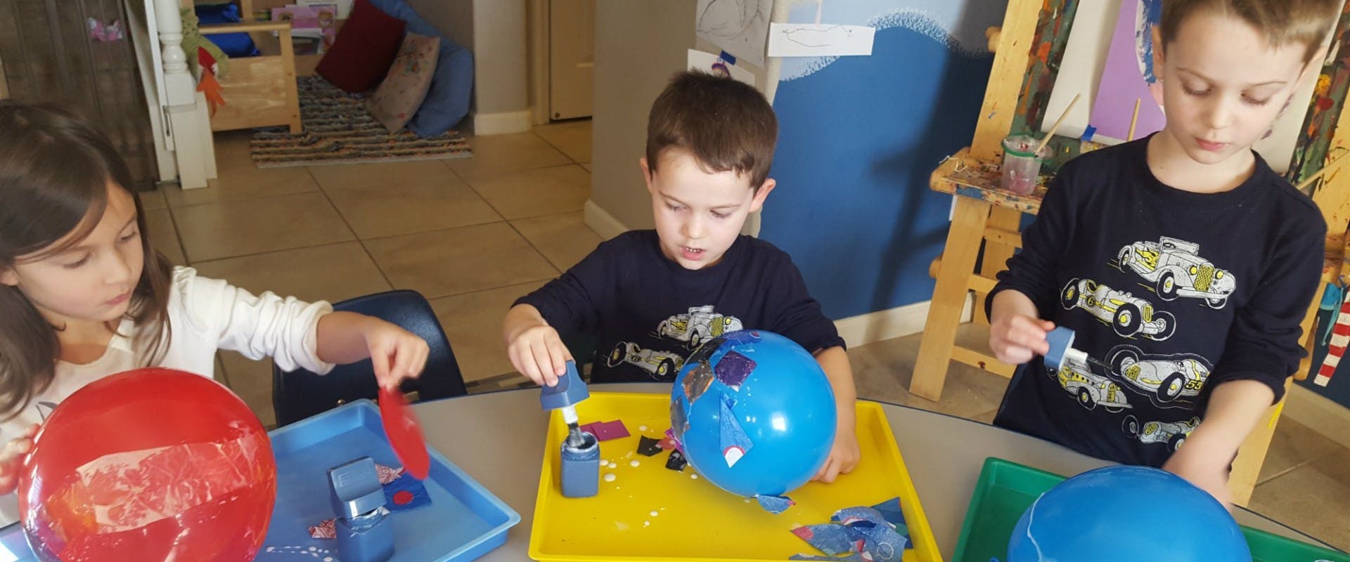 Three children playing with balloons and small objects at a table