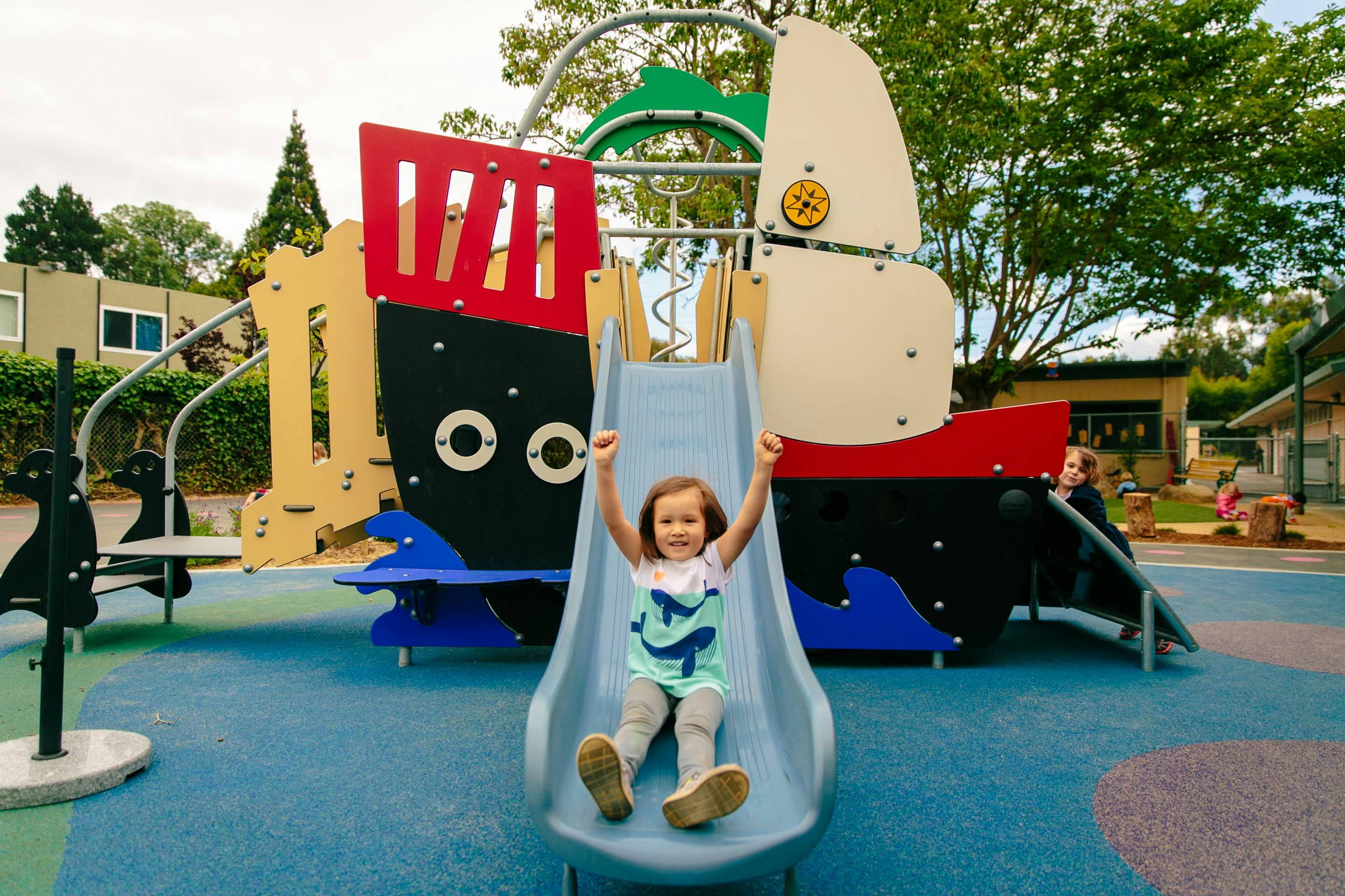 Child on a slide with arms raised on a playground