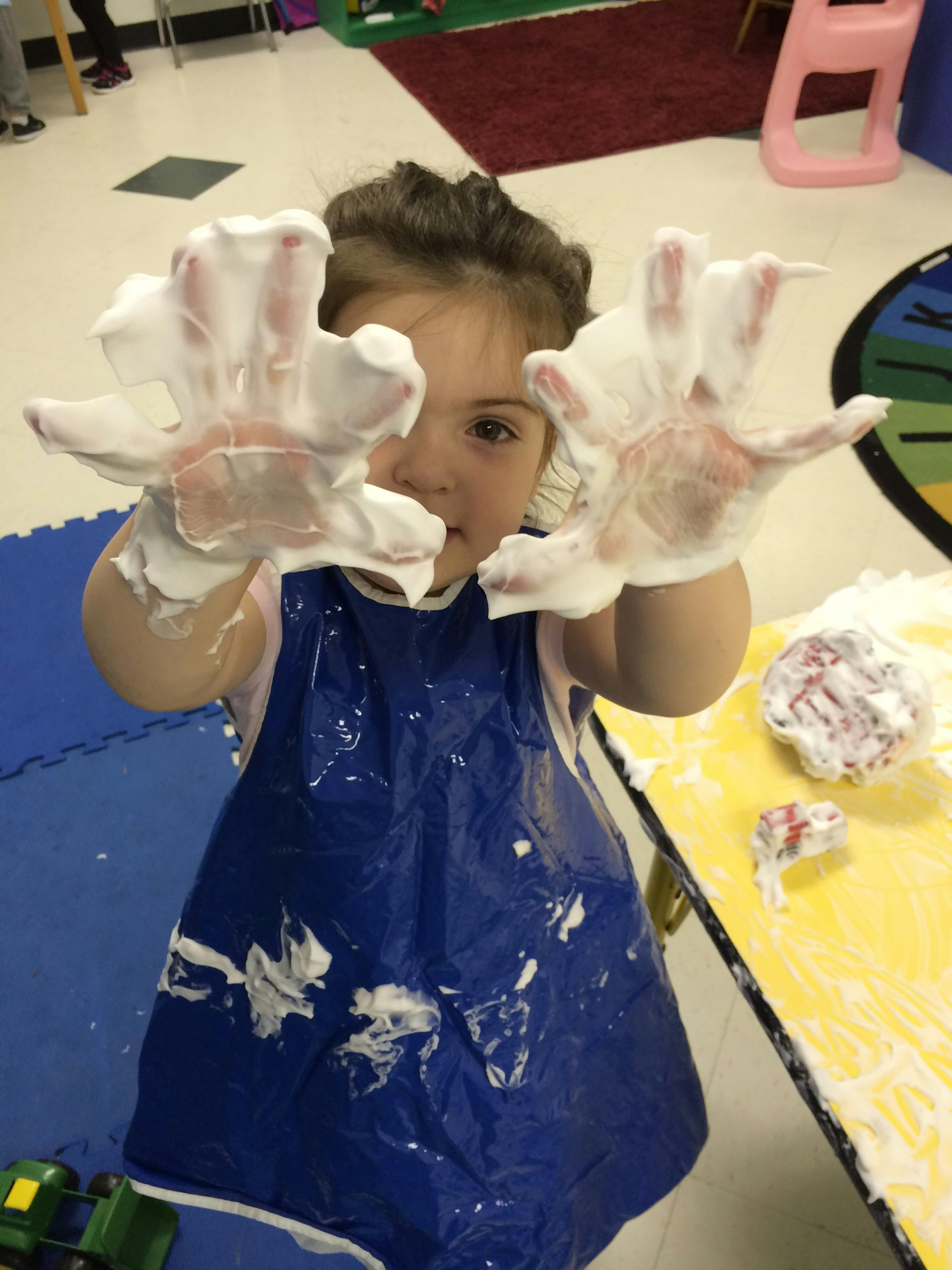 Child with hands covered in foam, wearing a blue smock