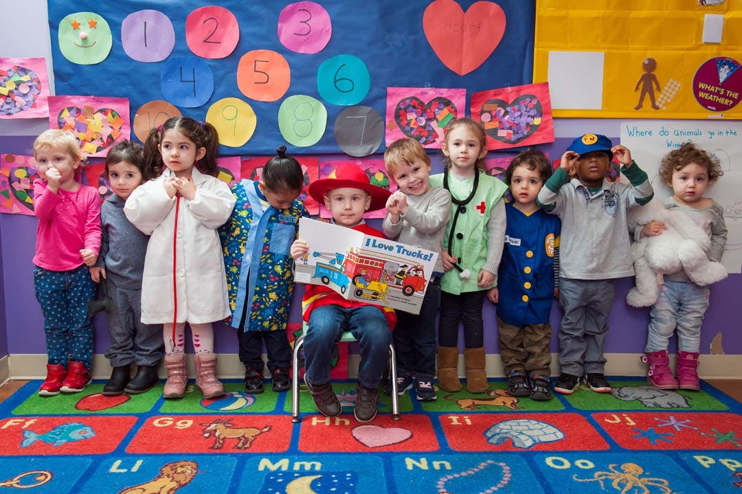 Children in costumes posing with one child holding a book in a classroom
