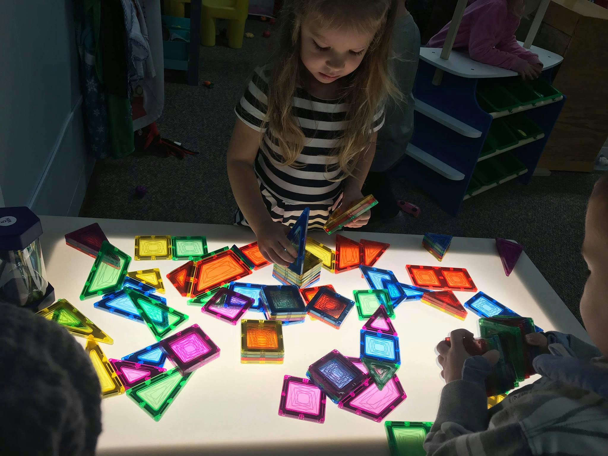 Child playing with colorful translucent magnetic tiles on a light table