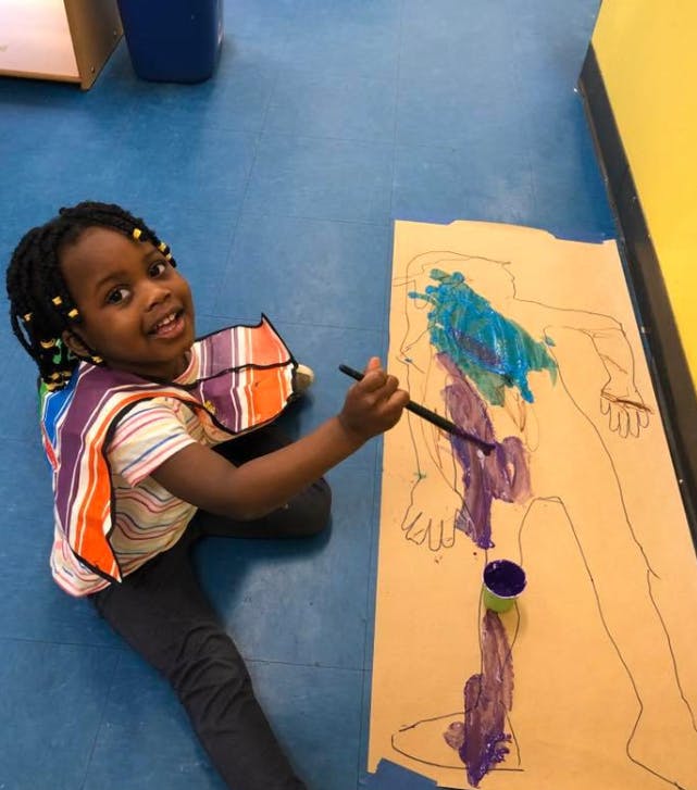 Child painting on a large paper outline of a person