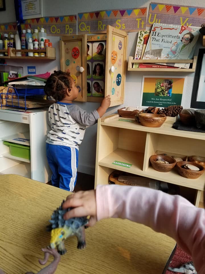 Child opening a wooden cabinet in a classroom