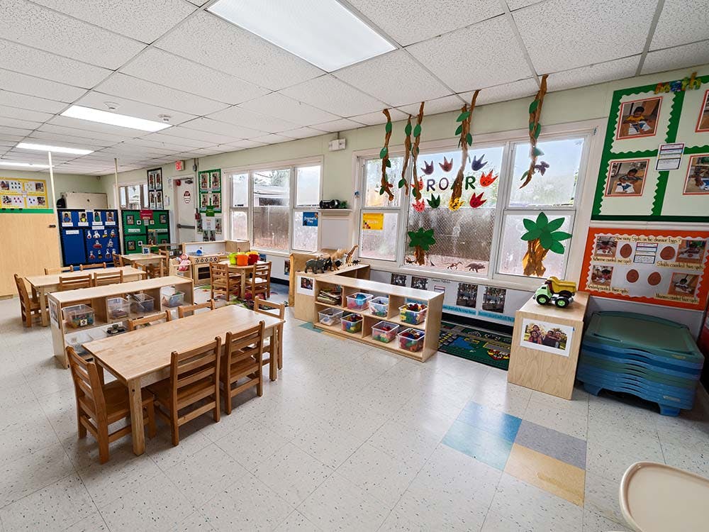 Empty classroom with small wooden tables and chairs, and windows decorated with leaves