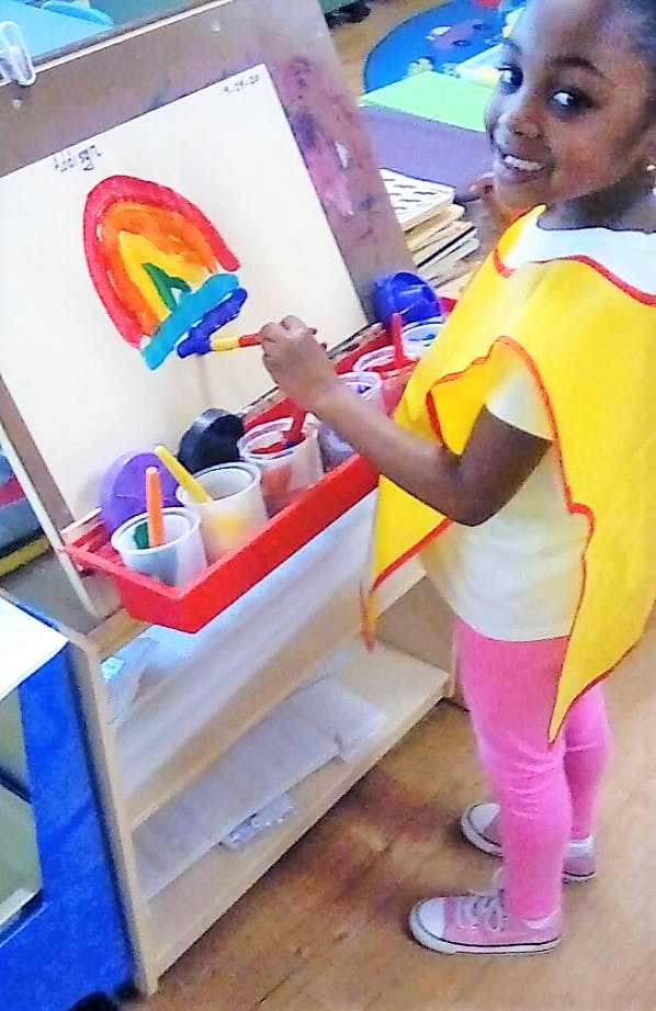 Child painting a rainbow on an easel in a classroom