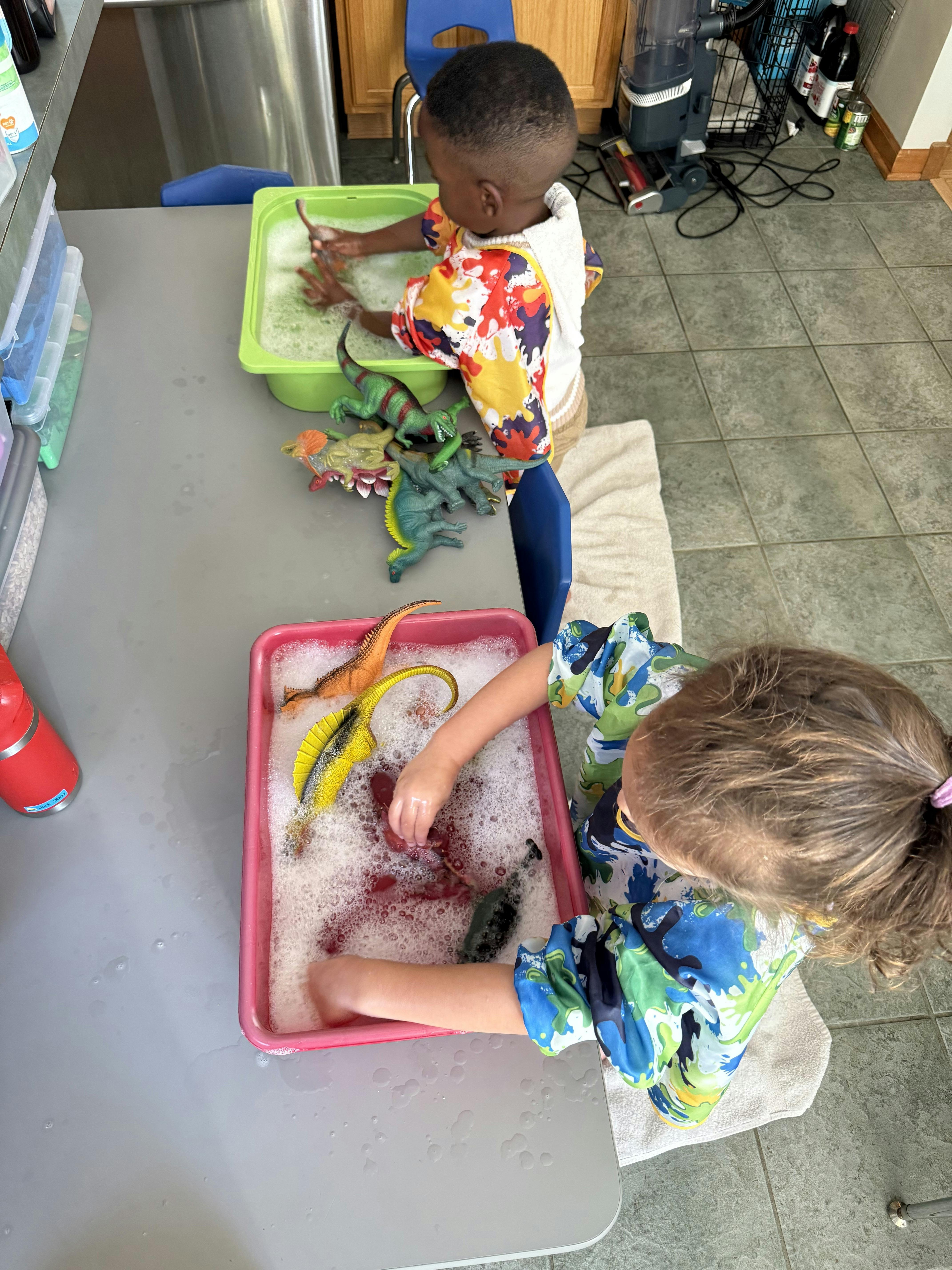 Two children playing with toys in soapy water in plastic bins