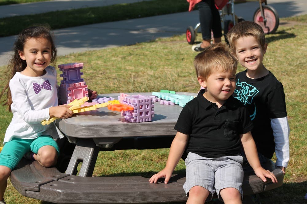 Three children playing with building blocks at a picnic table