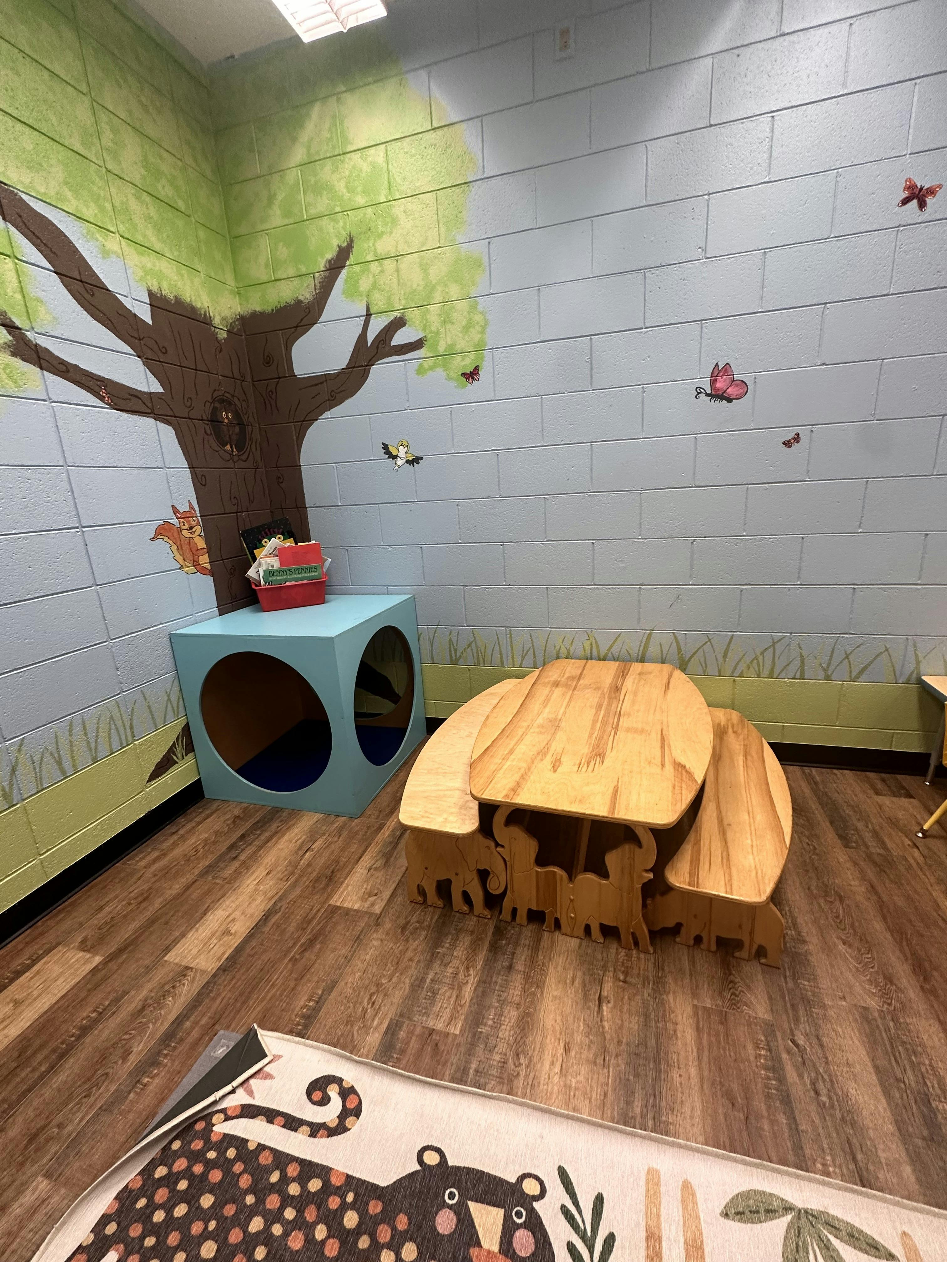 Children's play area with a tree mural, wooden table, and blue cube