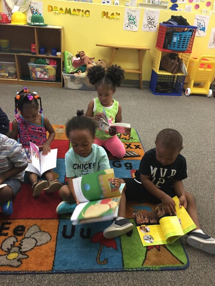 Four children sitting on a rug reading books in a classroom