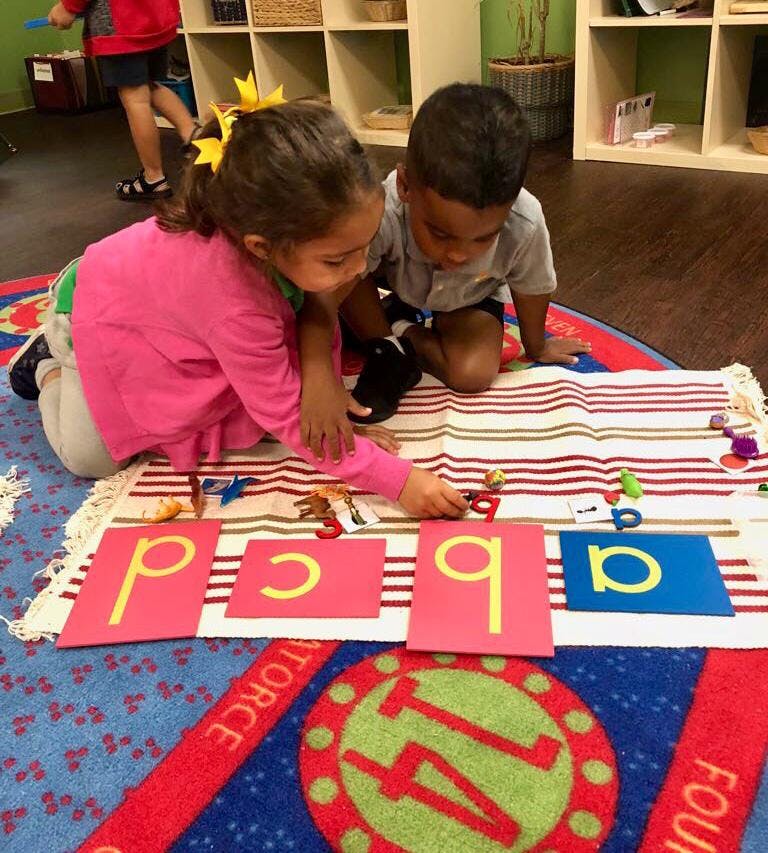 Two children playing with letter cards and small objects on a rug