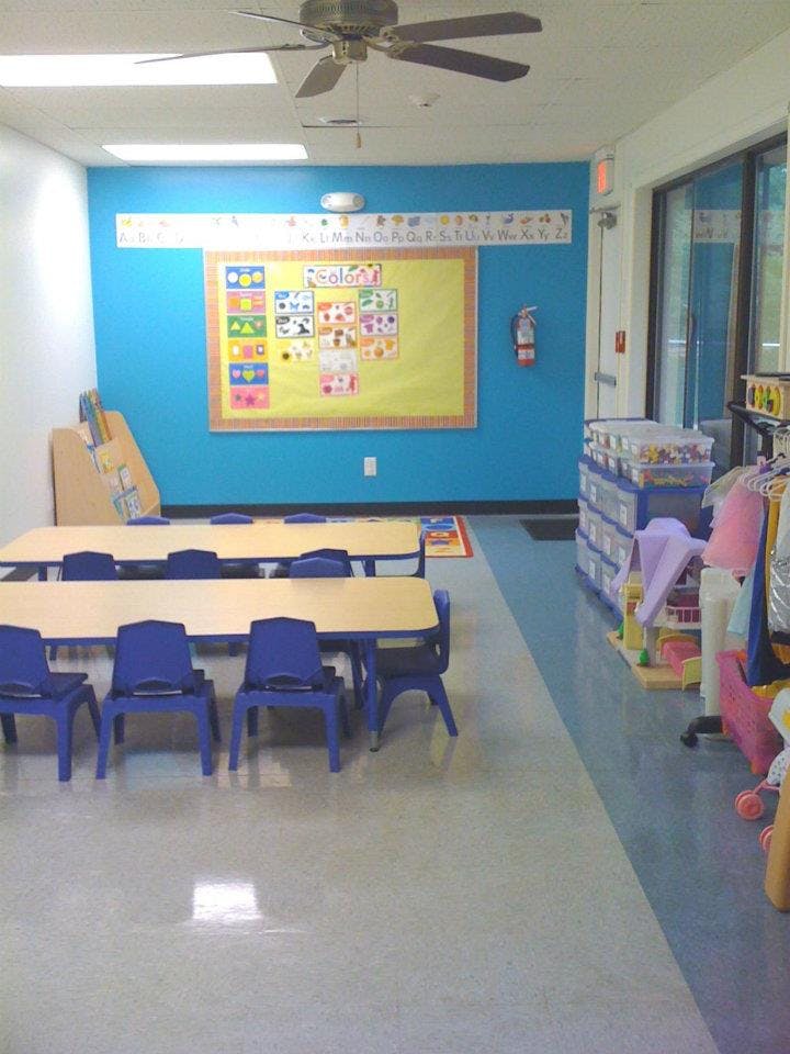 Classroom with small tables and chairs, a bulletin board on a blue wall