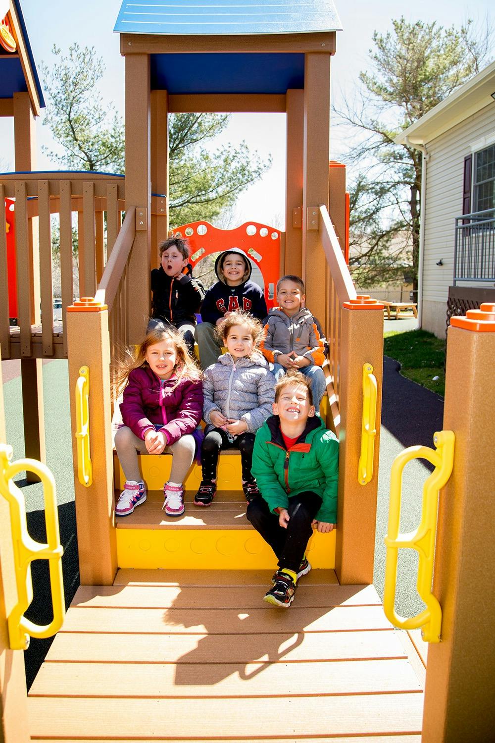 Six children sitting on the steps of a playground structure