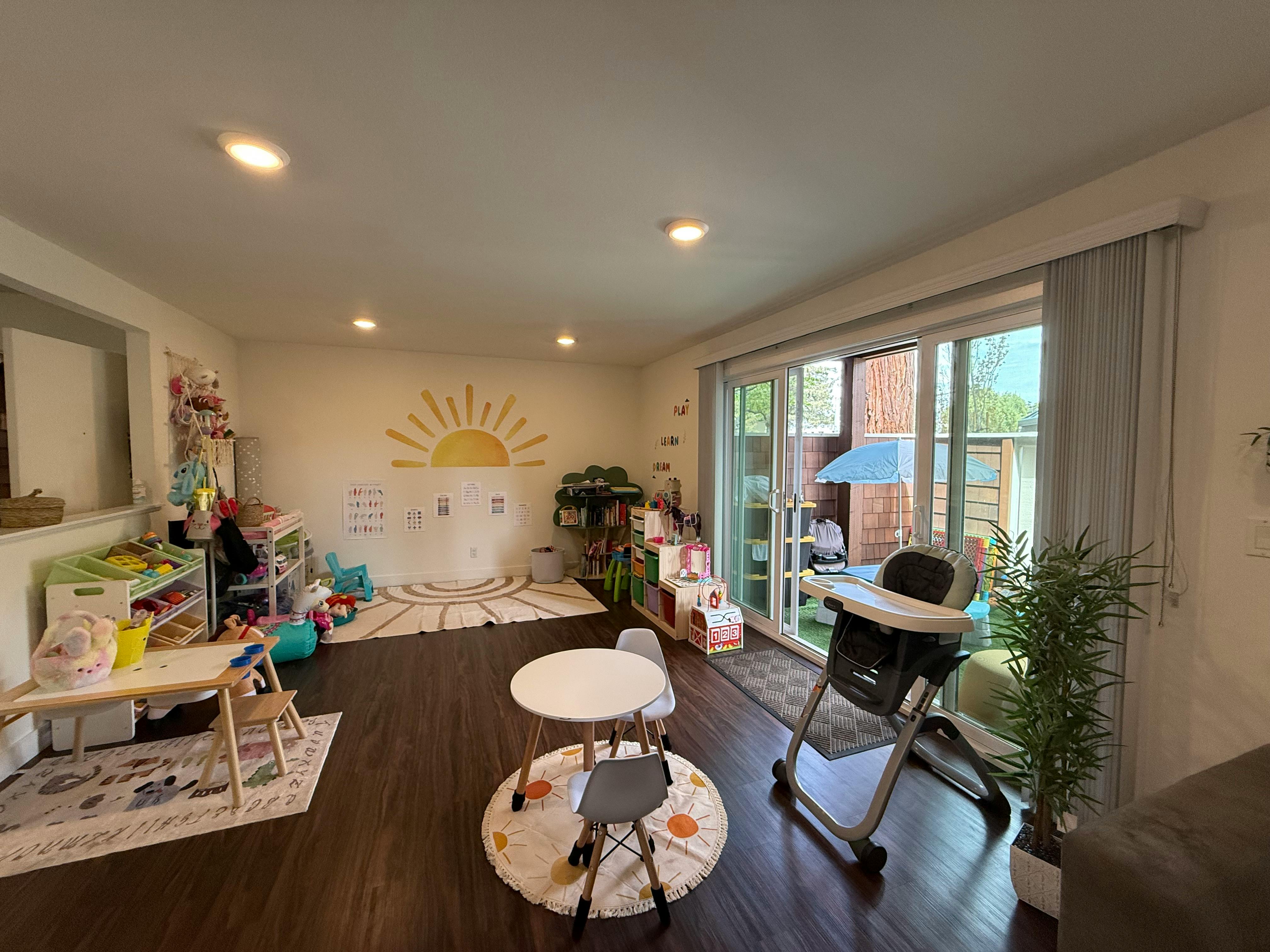 Playroom with small tables and chairs, toys, and a sun mural on the wall
