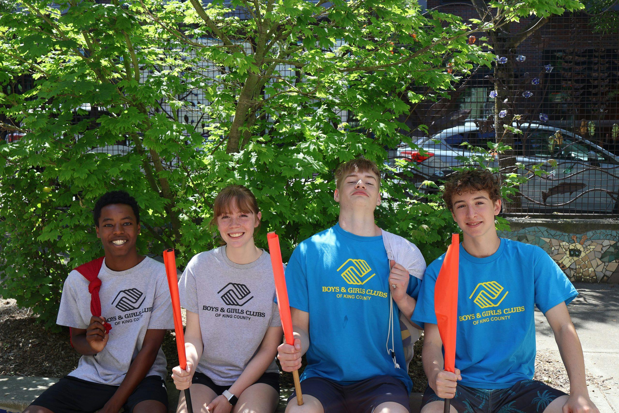 Four teens holding orange flags, Boys & Girls Clubs of King County logo on shirts