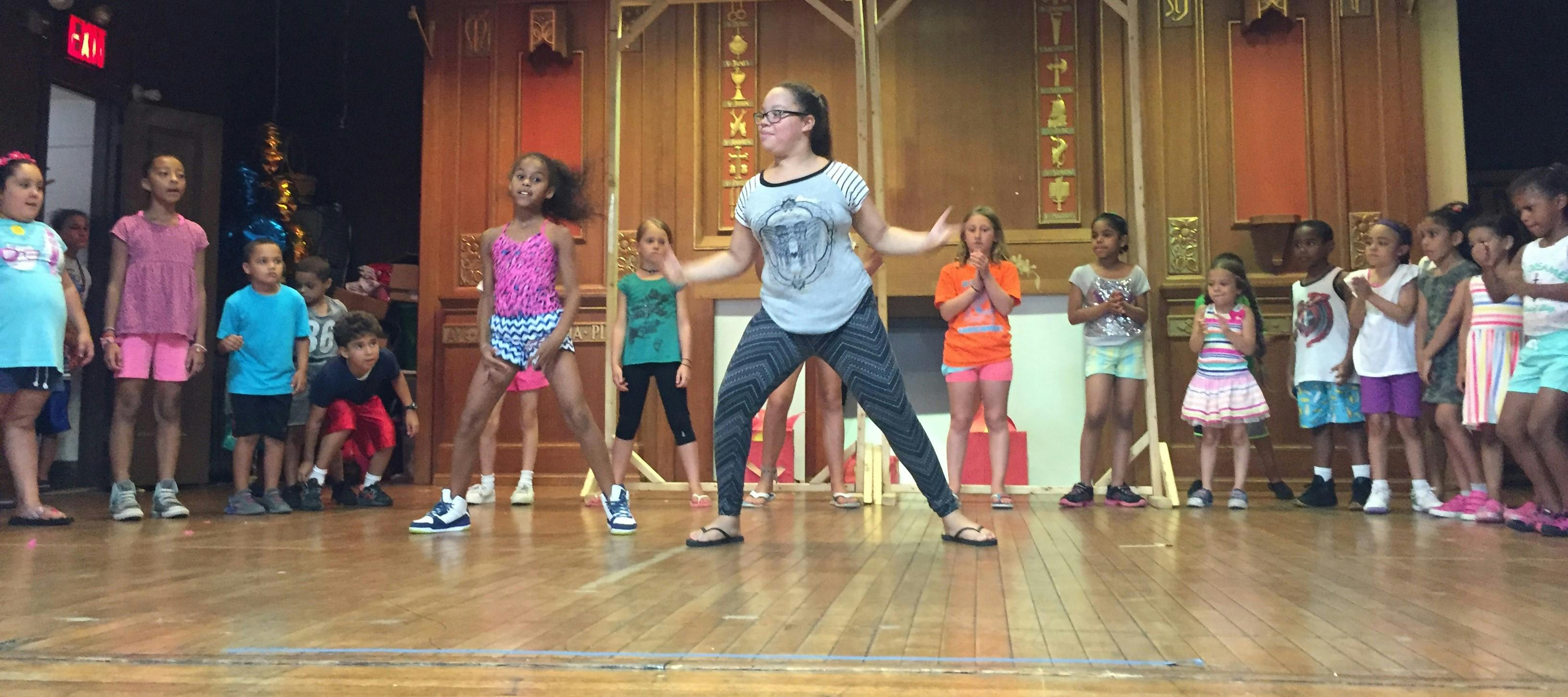 Person leading a group of children in a dance class on a stage