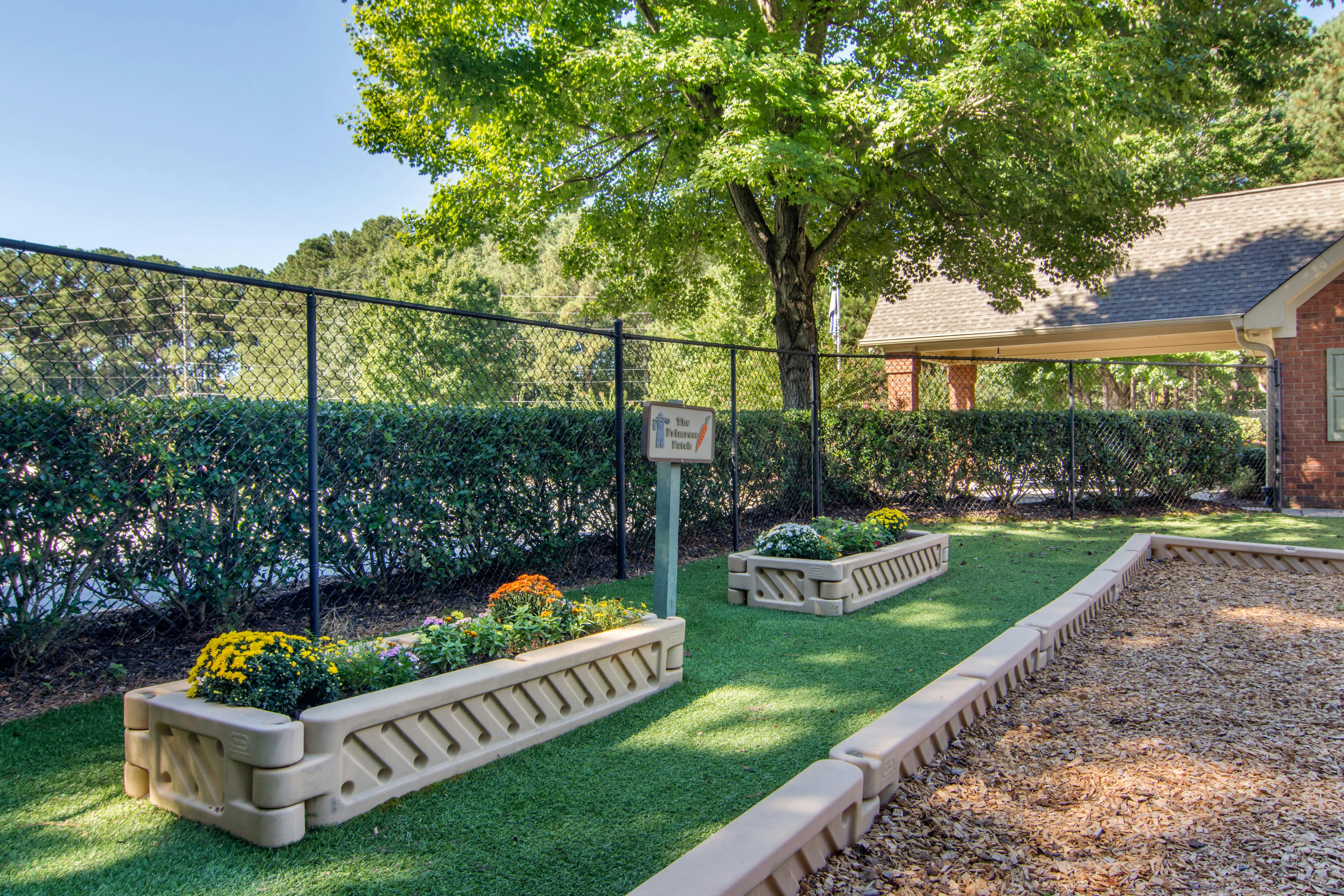 Raised garden beds with flowers on artificial turf, next to a wood chip area