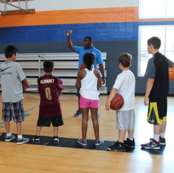 Adult teaching basketball to children in a gym