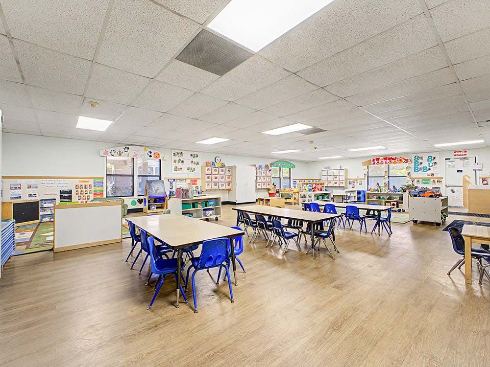 Empty classroom with tables and chairs arranged, children's artwork on walls