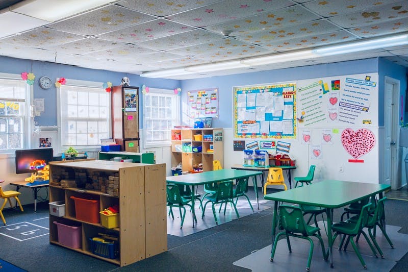 Classroom with small green tables and chairs, storage shelves, and decorated walls