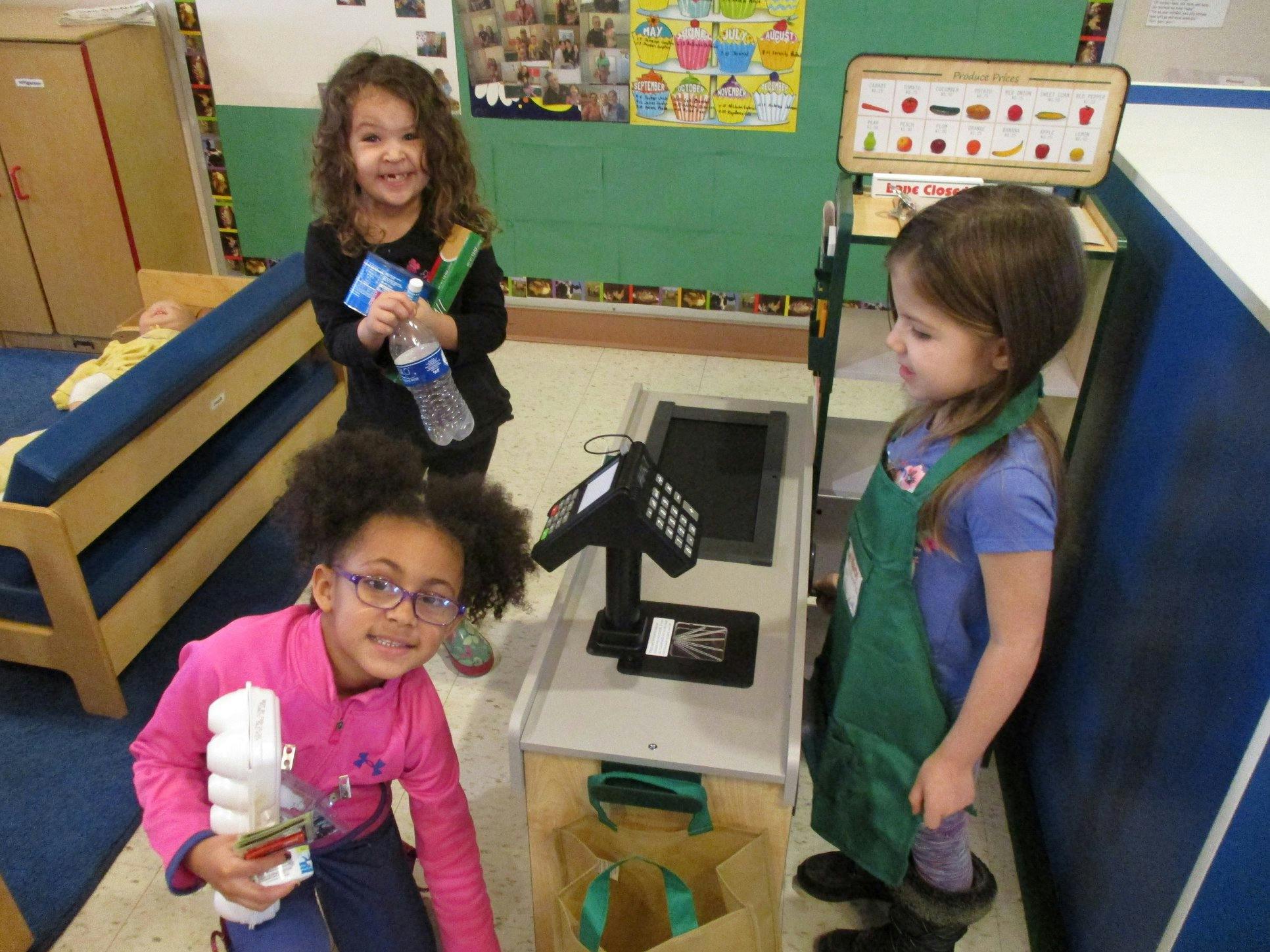 Three children playing with a toy cash register and groceries