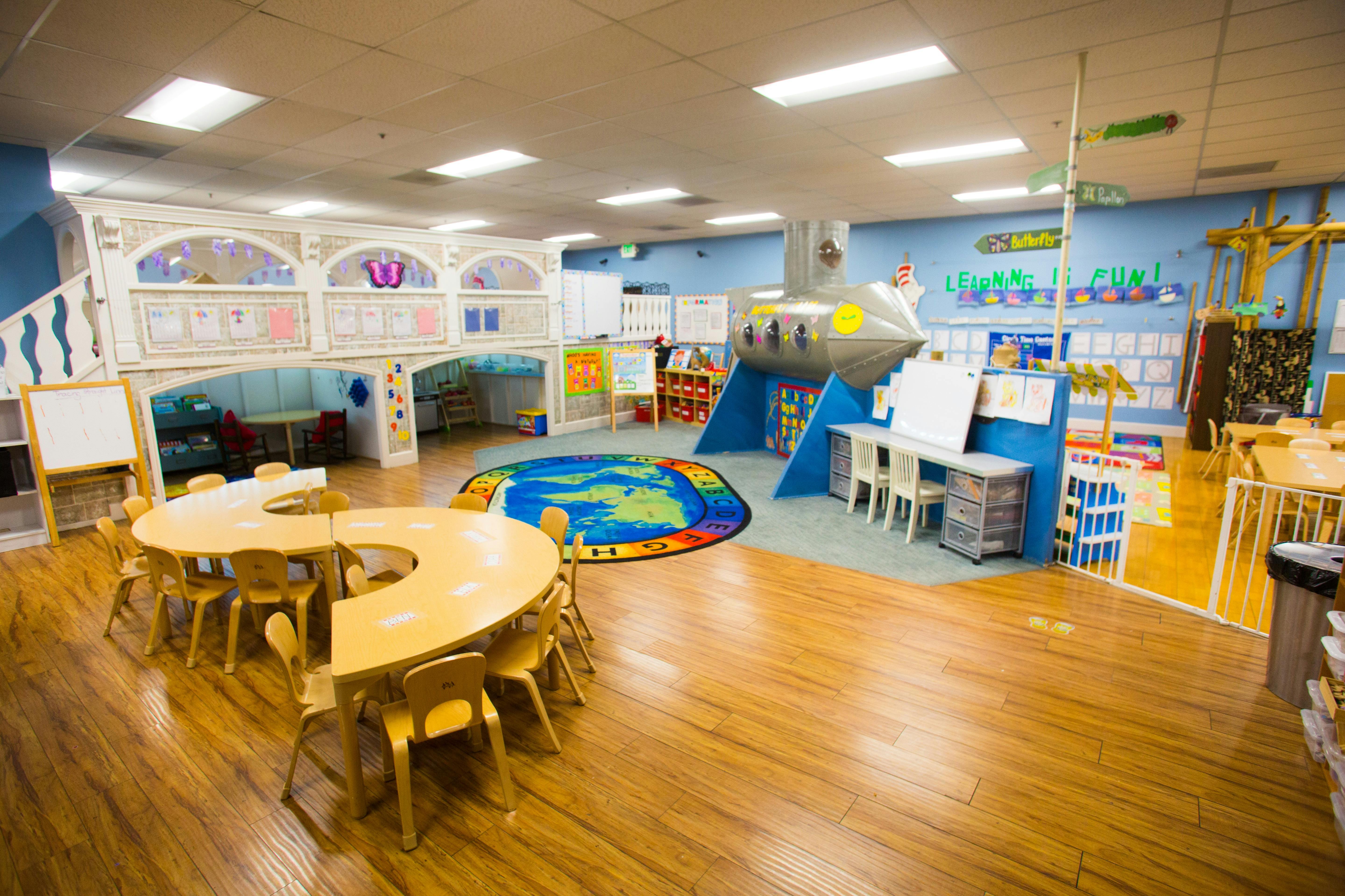 Playroom with tables and chairs, a play structure, and a colorful rug