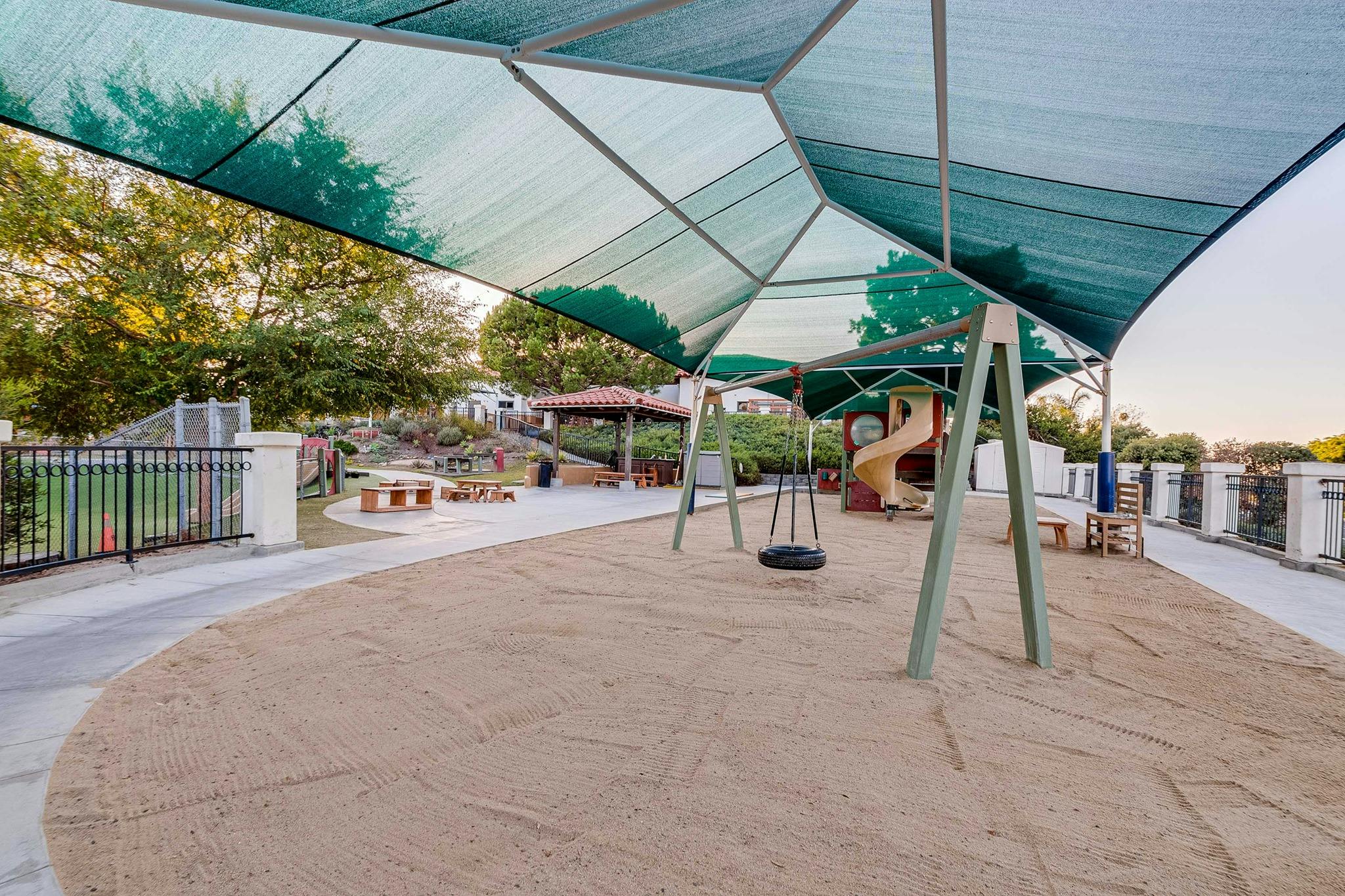 Playground with sand, swings, and a slide under a large shade structure