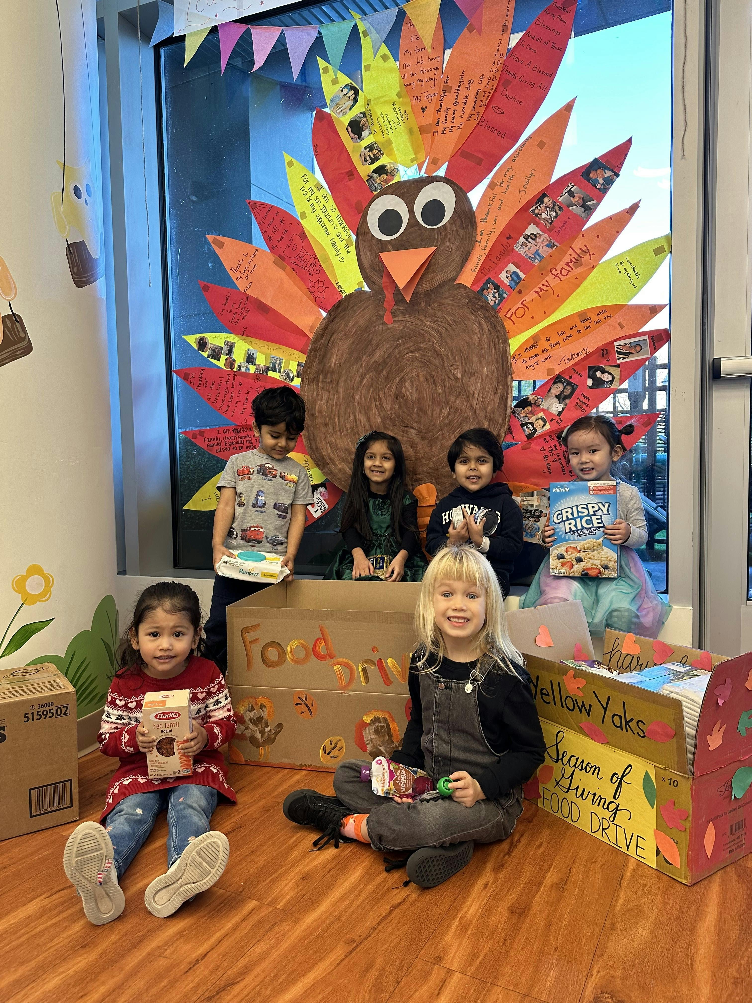 Children with food donations in front of a large paper turkey decoration