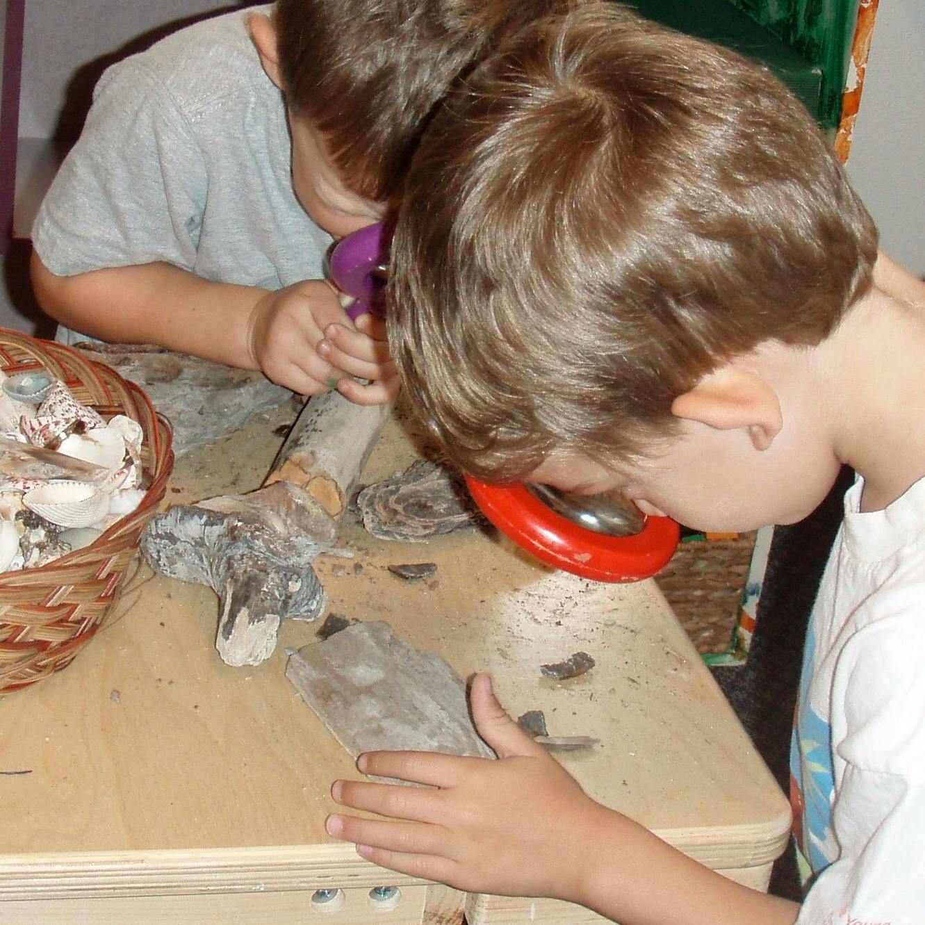 Two children looking through magnifiers at objects on a table