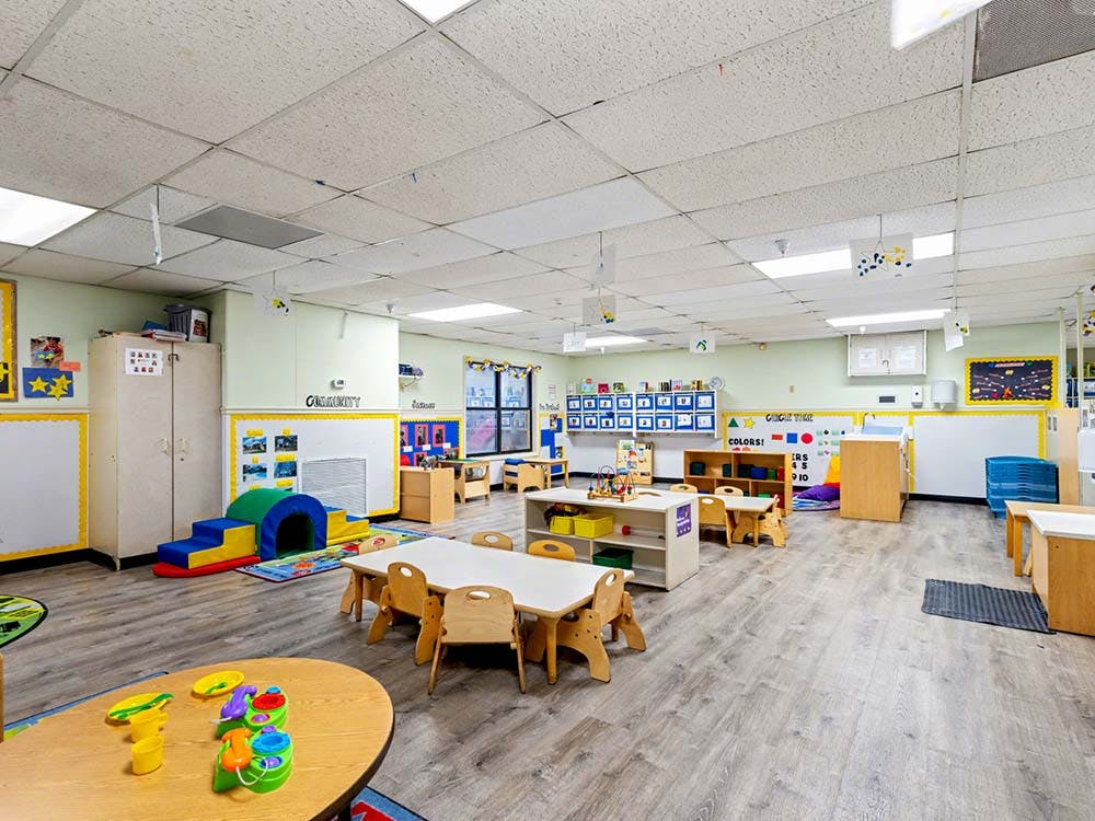 A colorful empty classroom with small tables, chairs, and play equipment