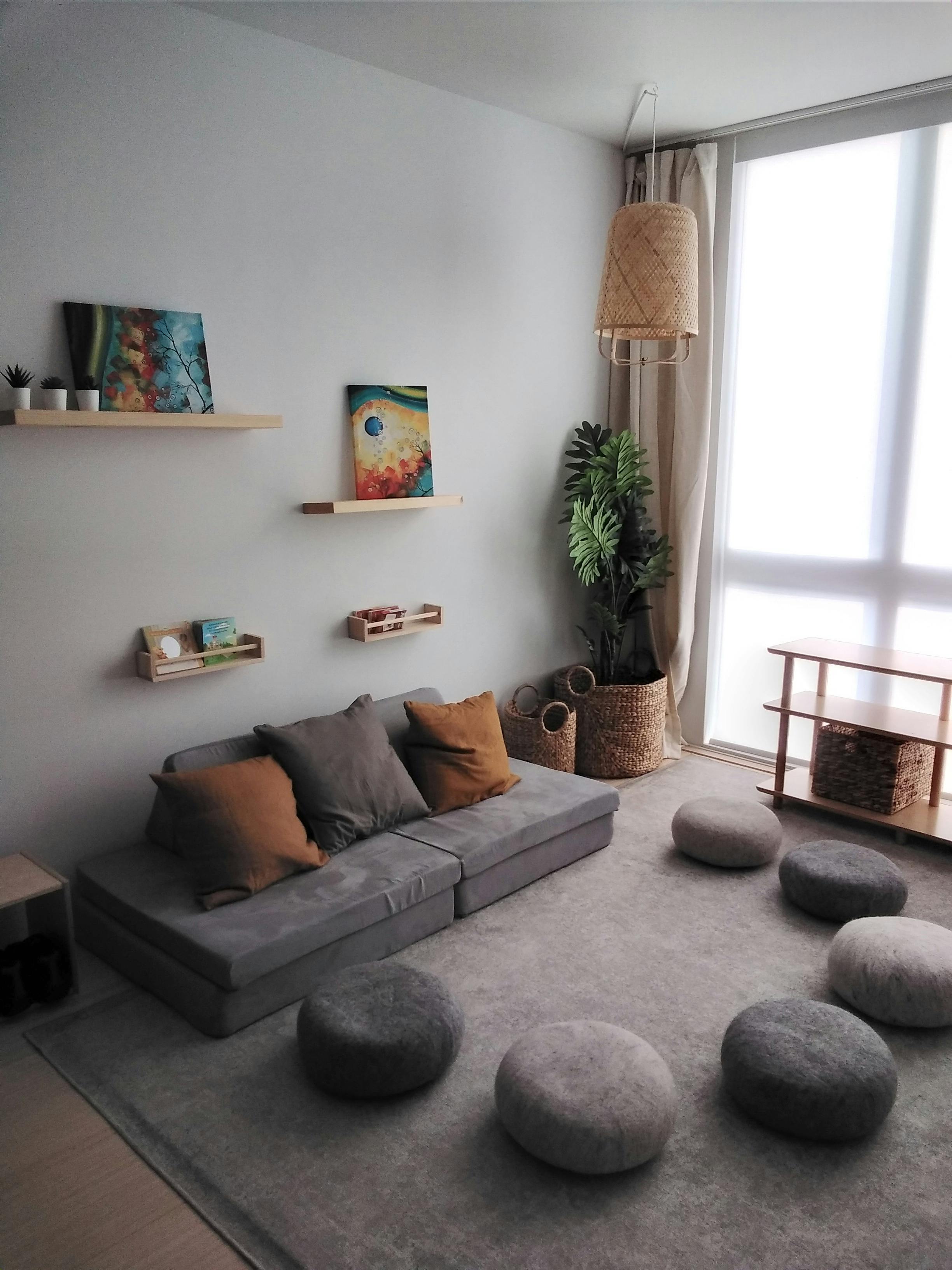 Living room with a gray sectional sofa, floor cushions, and wall shelves