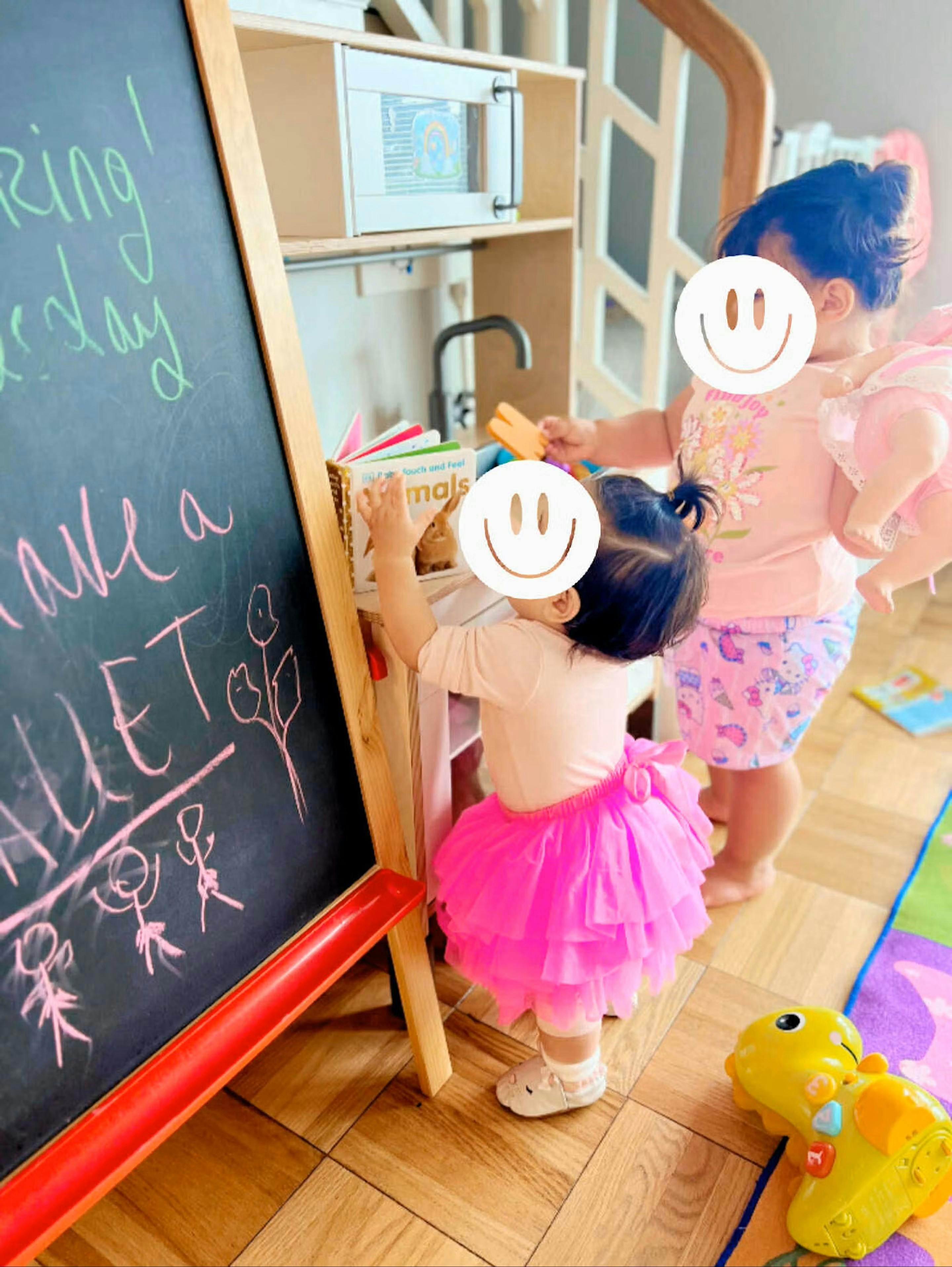 Two children playing in a play kitchen, one holding a book