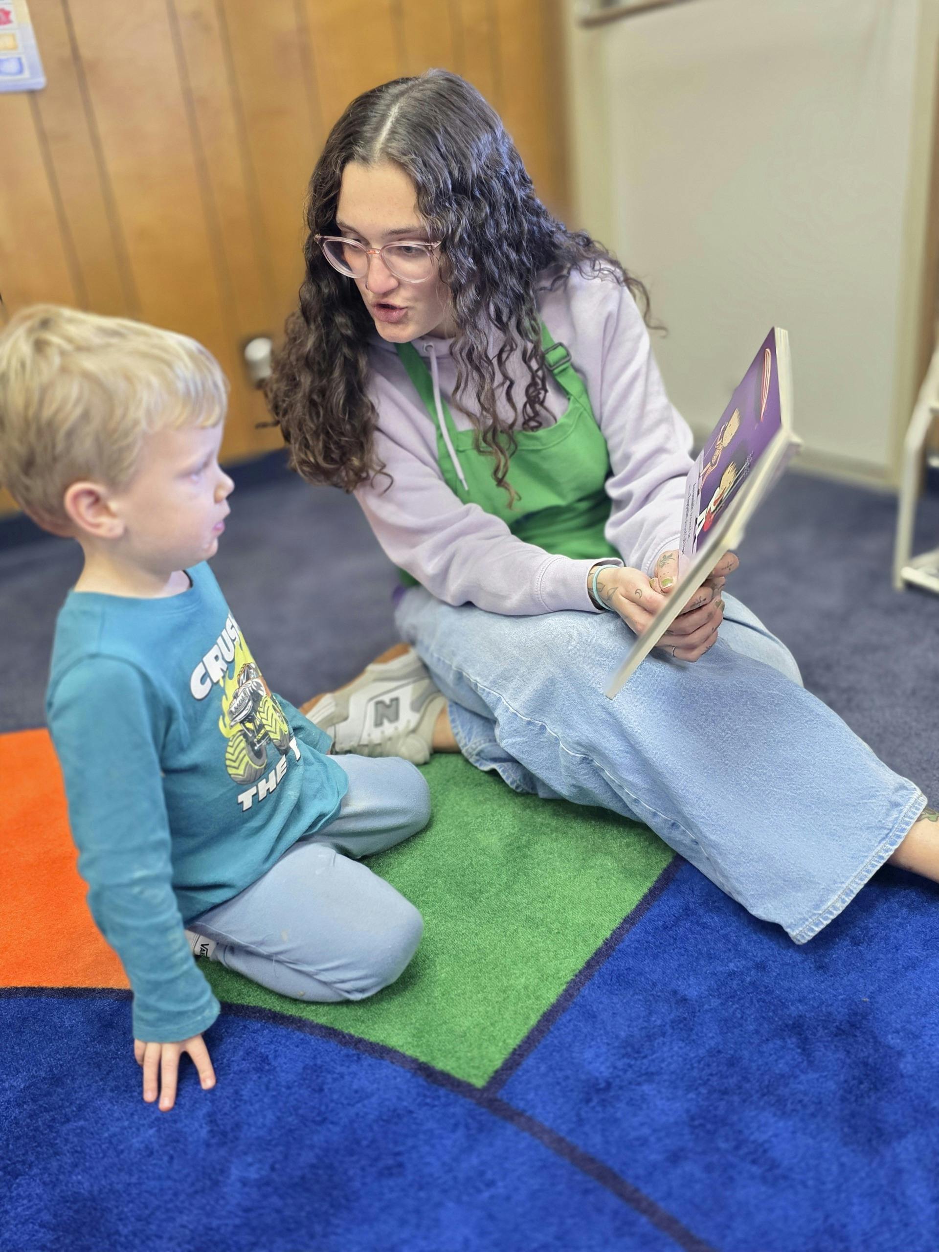 Person with glasses reading a book to a child in a classroom