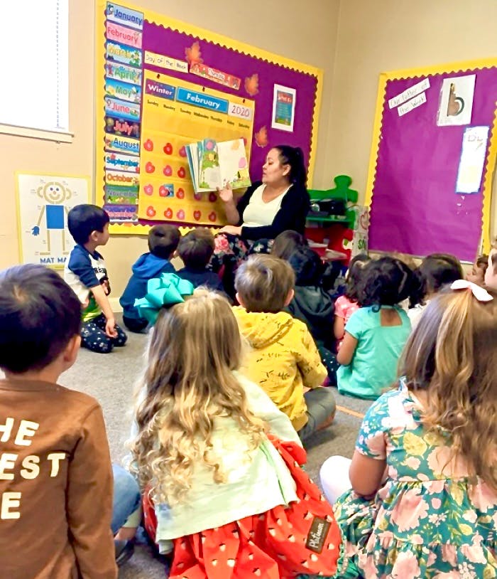 Adult reading a book to a group of children in a classroom