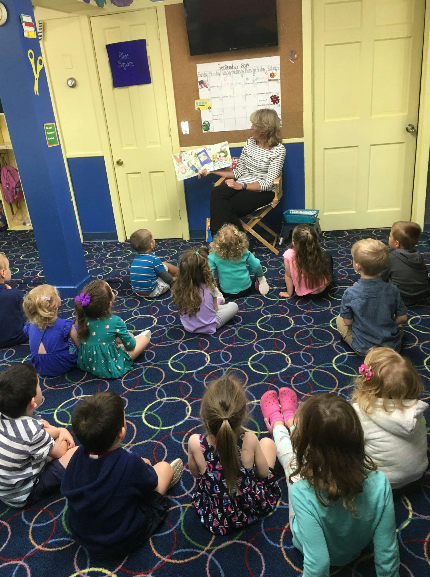 Adult reading a book to a group of children in a classroom