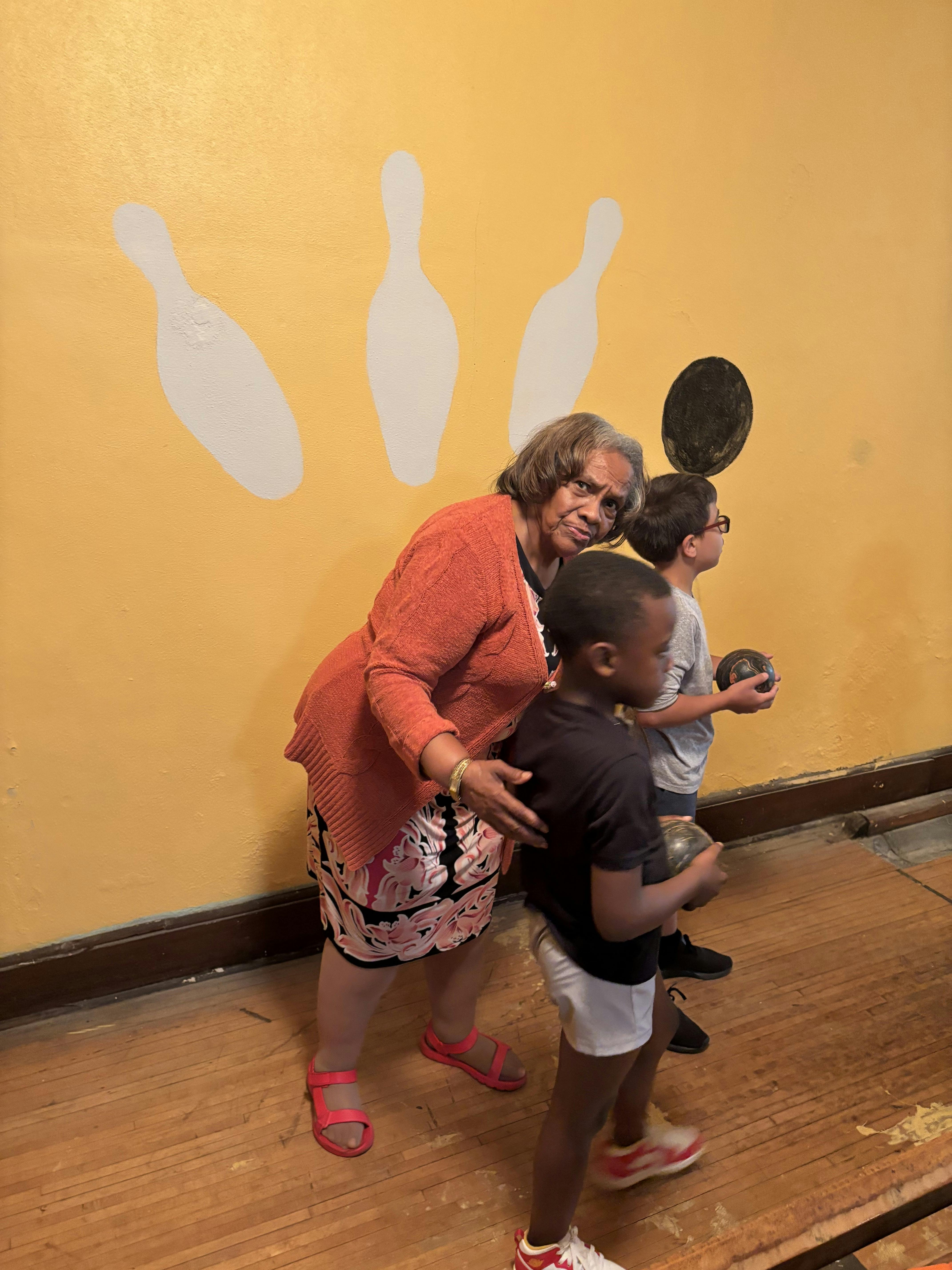 Adult and two children holding bowling balls in front of a bowling themed wall