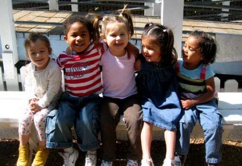 Five children sitting on a bench with arms around each other