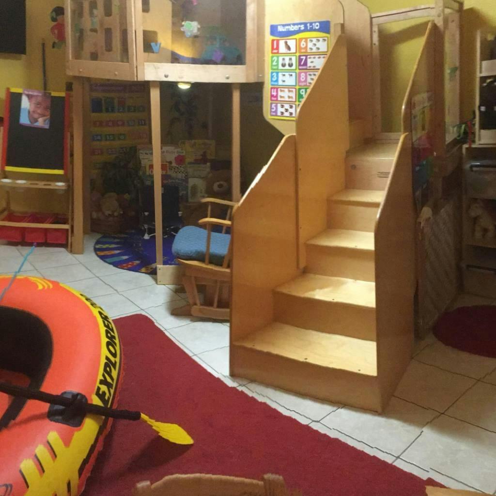 Wooden play structure with stairs and an inflatable boat on a red rug