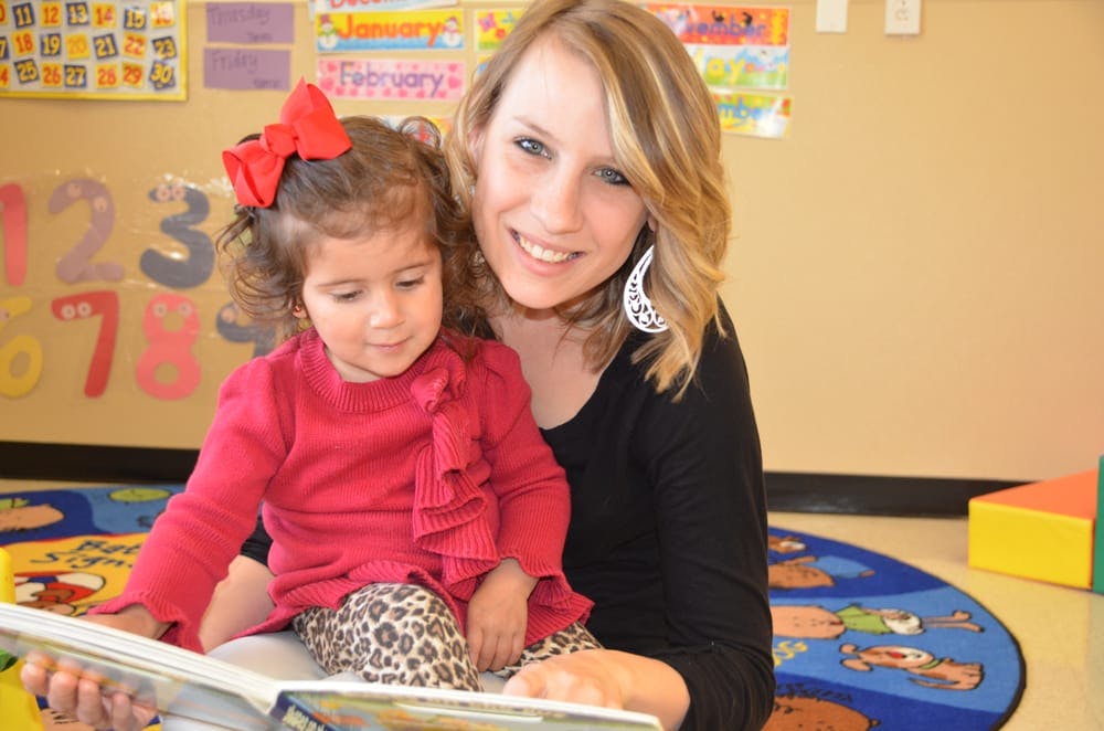 Person and child reading a book together in a classroom