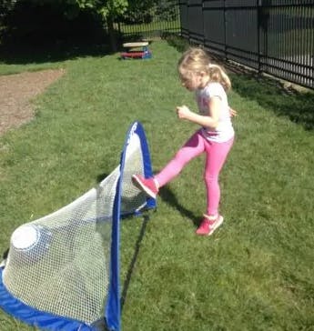 Child kicking a soccer ball into a small net on grass
