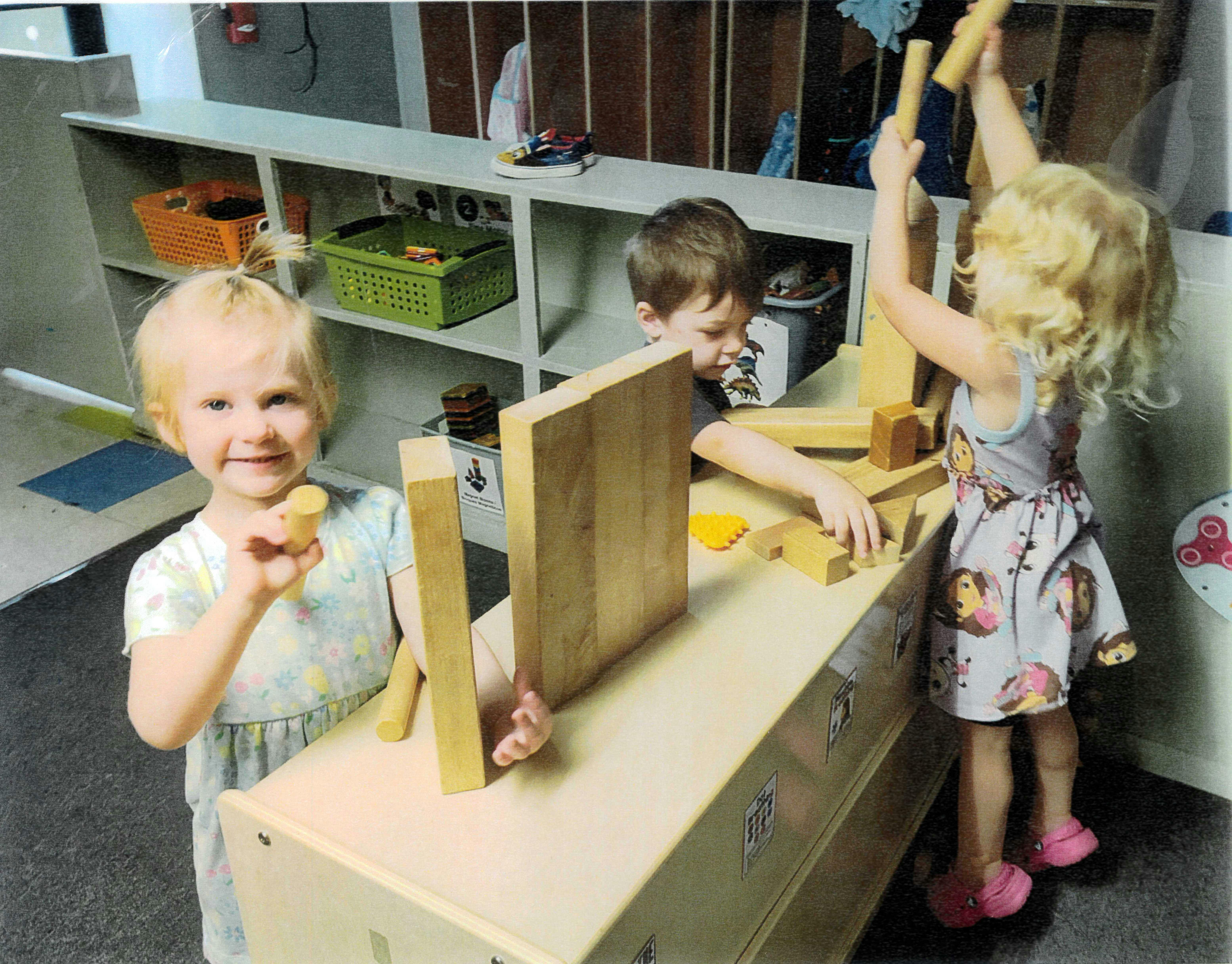 Children playing with wooden blocks at a table in a classroom